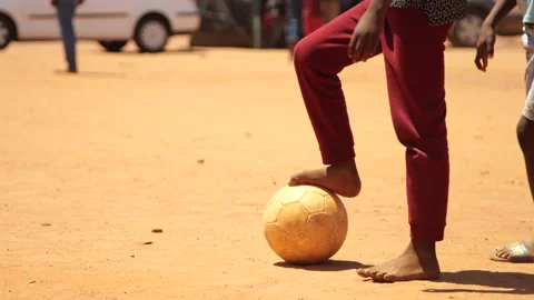 Medium close-up of young boy standing with his bare foot on soccer ball in Video stock 138812864