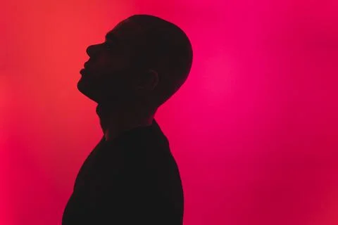Medium closeup side shot of a young bald man looking up over the pink background Stock Photos