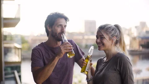 Medium front view shot of cheerful young couple enjoying a beer while hanging Stock Footage 277969884