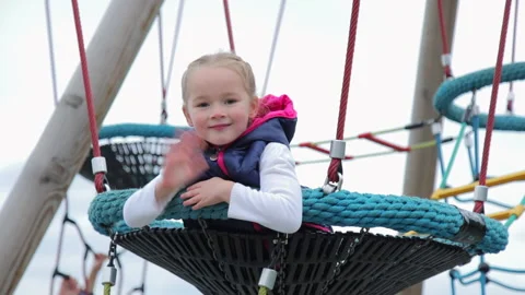 Medium full shot of a little cute Caucasian child girl who sits on a round swing Stock Footage 185684727