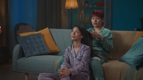 Medium-full video capturing two young women wearing pajamas sitting on the couch Stock Footage 252210328