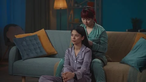 Medium-full video capturing two young women wearing pajamas sitting on the couch Stock Footage 252210623