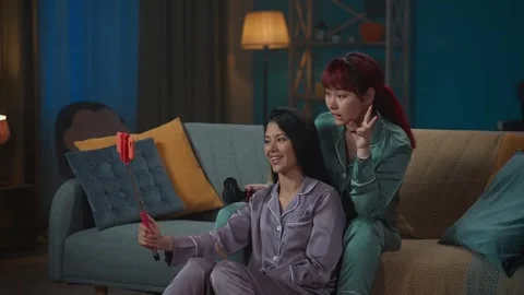 Medium-full video capturing two young women wearing pajamas sitting on the couch Stock Footage 252210964