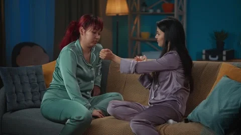 Medium-full video capturing two young women wearing pajamas sitting on the couch Stock Footage 252214674