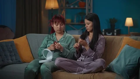 Medium-full video capturing two young women wearing pajamas sitting on the couch Stock Footage 252214780