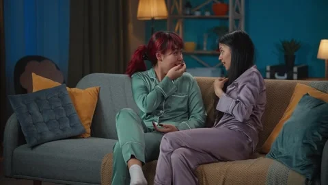 Medium-full video capturing two young women wearing pajamas sitting on the couch Stock Footage 252216182
