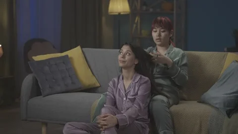Medium-full video capturing two young women wearing pajamas sitting on the couch Stock Footage 252222182