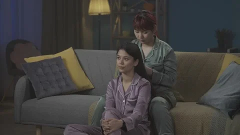 Medium-full video capturing two young women wearing pajamas sitting on the couch Stock Footage 252222608