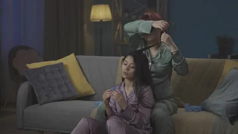Medium-full video capturing two young women wearing pajamas sitting on the couch Stock Footage 252222900