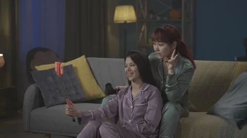 Medium-full video capturing two young women wearing pajamas sitting on the couch Stock Footage 252223166