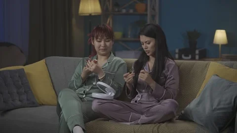 Medium-full video capturing two young women wearing pajamas sitting on the couch Stock Footage 252228977