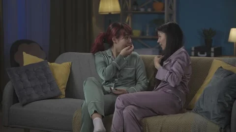 Medium-full video capturing two young women wearing pajamas sitting on the couch Stock Footage 252230743