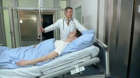 Medium lockdown shot of two doctors pushing a patient on a hospital gurney into Stock Footage 10701428