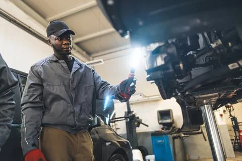 Medium low angle shot of a mechanic checking a car with a light. Repair shop Stock Photos