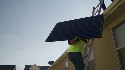 Medium panning low angle shot of workers carrying solar panel on roof / Stock Footage
