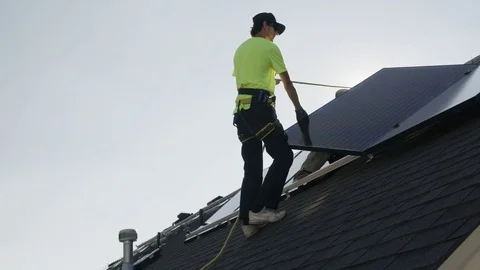 Medium panning low angle shot of workers installing solar panel on roof / Stock Footage 77469305