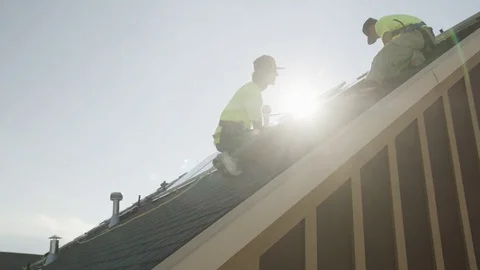 Medium panning low angle shot of workers installing solar panel on roof / Stock Footage 77469343
