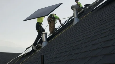 Medium panning low angle shot of worker carrying solar panel on roof / Mapleton, Stock Footage 77469537