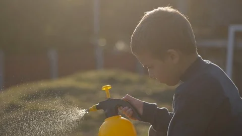 Medium plan a boy from a sprayer sprays the grass in the sun's glare Vídeos de archivo 129185346