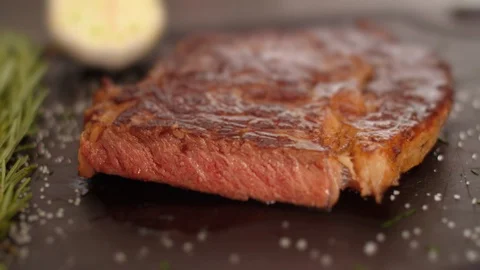 Medium Rare beef steak be on a cutting Board with salt and a sprig of rosemary Stock Footage 124672797