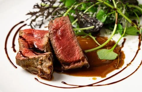 Medium rare beef steak with green leaves salad and sauce. Close up. Stock Photos
