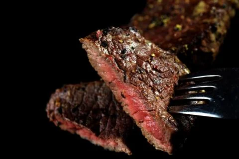 Medium rare beef steak piece on a fork . Spiced with peppercorns and herbs. Stock Photos