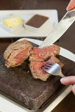 Medium rare steak sizzling on hot stone plate being sliced Stock Photos