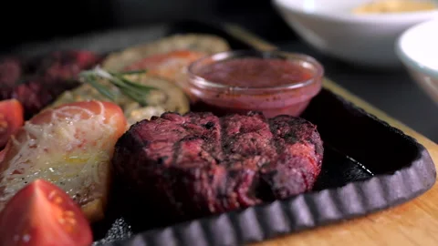 Medium-rare steak with vegetables, tomatoes and sauce on a cast iron tray Stock Footage 148119045
