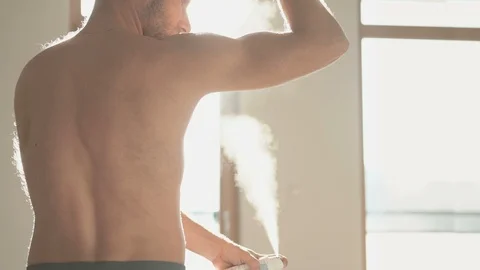 Medium shoot of the man spraying a lot to armpit deodorant spray backlit window  Stock-Footage 99070605