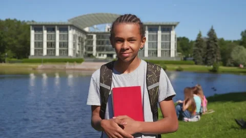 Medium shot of african student boy holding book and looking at camera at park. Stock Footage 157963133
