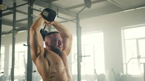 Medium shot of athletic man performing seated overhead tricep extension in gym Stock Footage 240077035