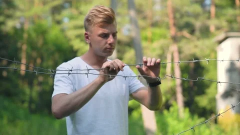 Medium shot of Attractive Blond Man touching barbed wire in prison. Stock Footage 157072658