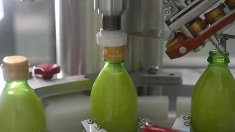 Medium shot of automatic bottling machine filling green fruit juice and capping Stock Footage 334274779