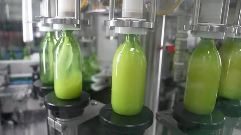 Medium shot of automatic bottling machine filling green fruit juice and capping Stock Footage 334274994