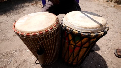 Medium shot of black man playing dundun with wooden sticks while sitting Stock Footage 113166409