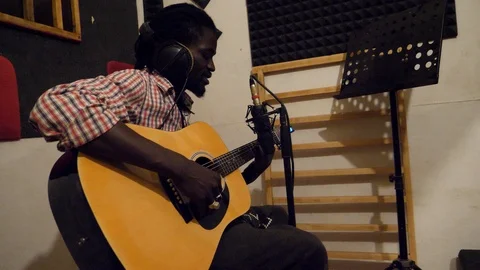 Medium shot of black man playing acoustic guitar sitting on chair in recording Video stock 116232970