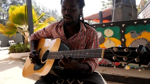 Medium shot of black man playing acoustic guitar sitting on chair Stock Footage 116234831
