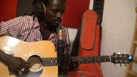 Medium shot of black man playing acoustic guitar sitting on chair in recording Video stock 116238914