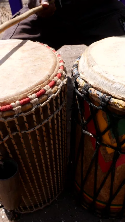 Medium shot of black man playing dundun with wooden sticks while sitting Stock Footage 230663818