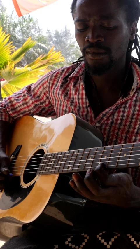 Medium shot of black man playing acoustic guitar sitting on chair Video stock 230664417
