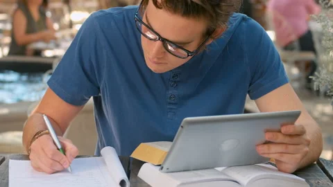 Medium shot of casually dressed student with tablet computer doing homework outd Stock Footage 199635087