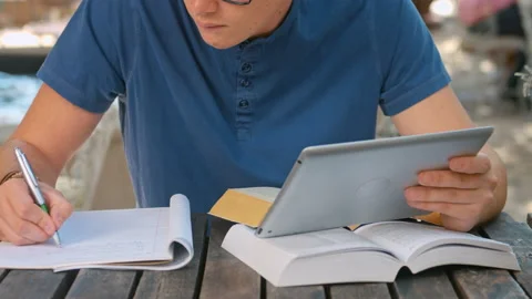Medium shot of casually dressed student with tablet computer doing homework outd Stockbeeldmateriaal 199635094