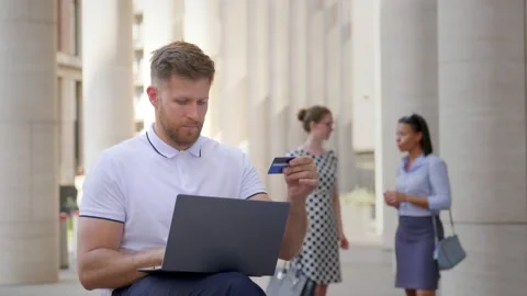Medium shot of caucasian businessman using laptop and credit card outdoors Stock Footage 157380130