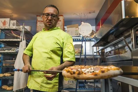 Medium shot of a chef with uniform holding a pizza near an oven Stock Photos