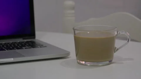 Medium shot of a clear glass coffee mug beside an open laptop on a clean white Stock Footage 346505533