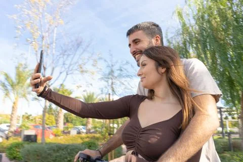 Medium shot a couple of lovers record themselves riding an electric scooter w Stock Photos