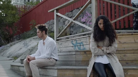 Medium shot of a couple on a tree bench after a fight. The young woman glancing Stock Footage 115578904