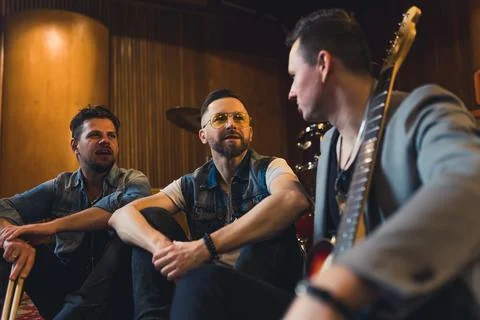 Medium shot of a drummer and two guitarists sitting on the floor and thinking Stock Photos