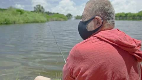 Medium shot of elderly man fishing on a lake while wearing a face mask Stock Footage 131058097