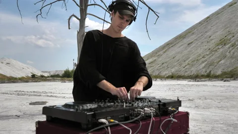 A medium shot of a guy mixing music at a DJ console in the middle of a desert Stock Footage 172296823